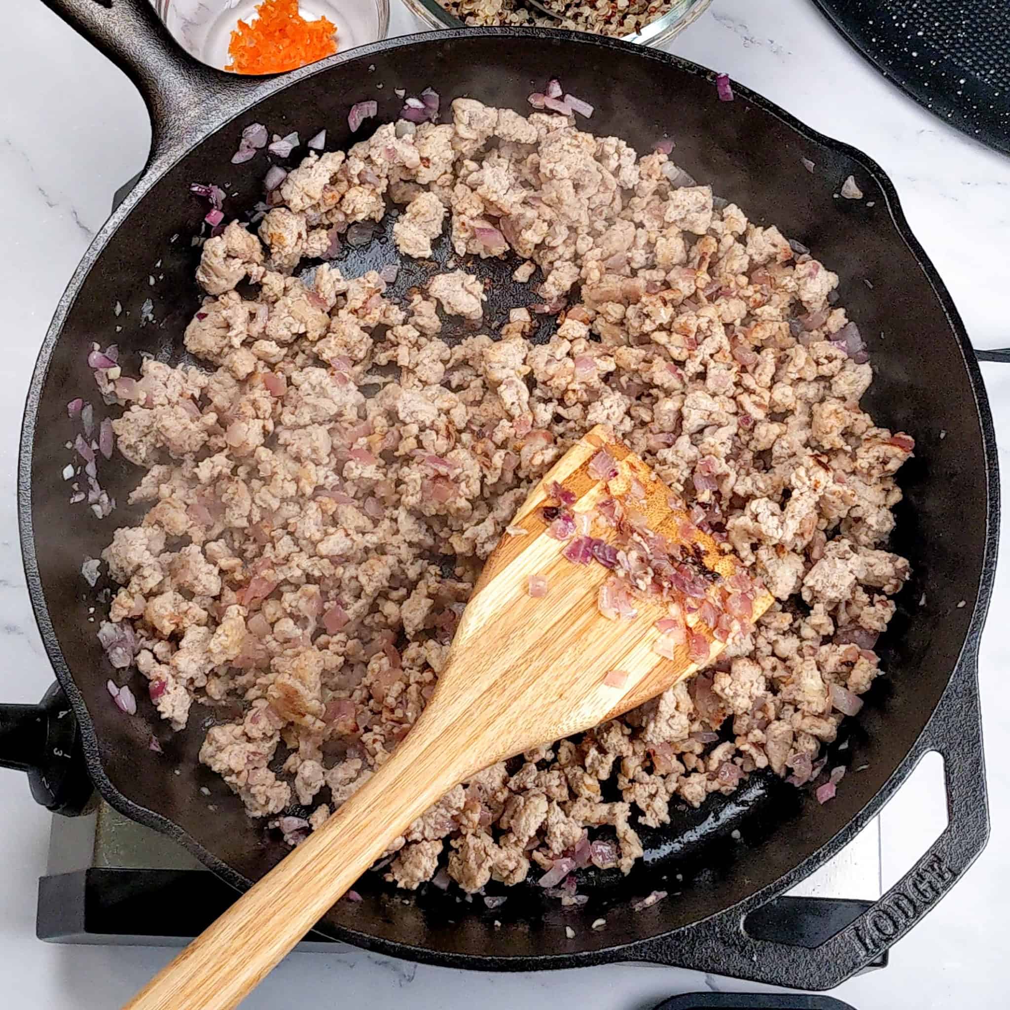 Cooked and crumbled ground turkey in a cast iron skillet with a wooden spatula.