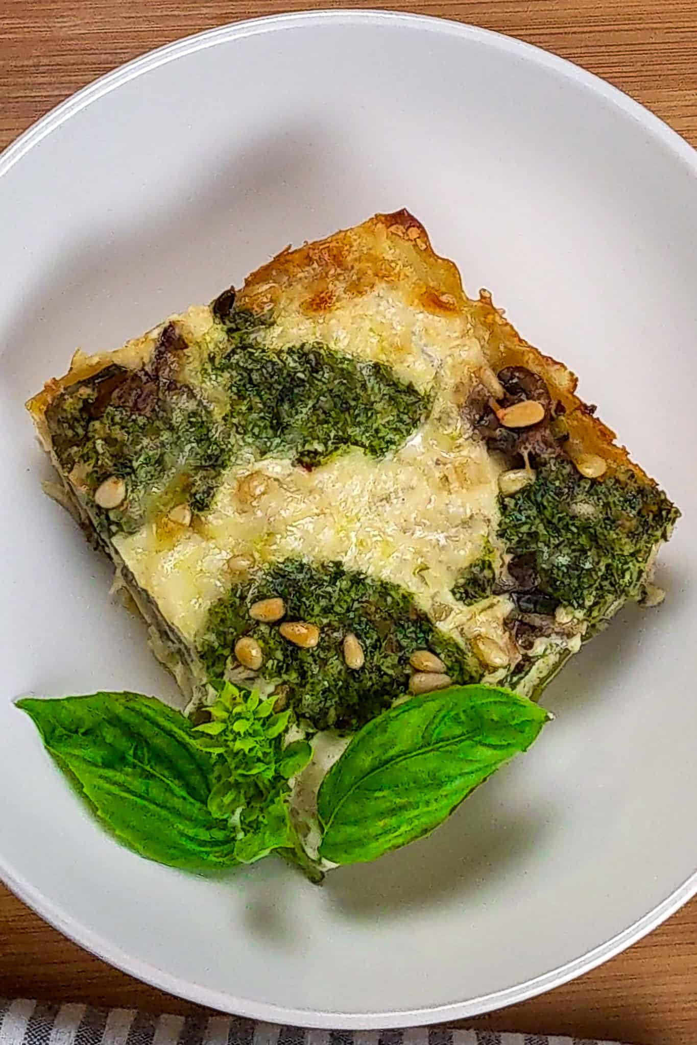 top view of the Creamy Spinach Pesto Mushroom Lasagna in a wide rim bowl garnished with basil.