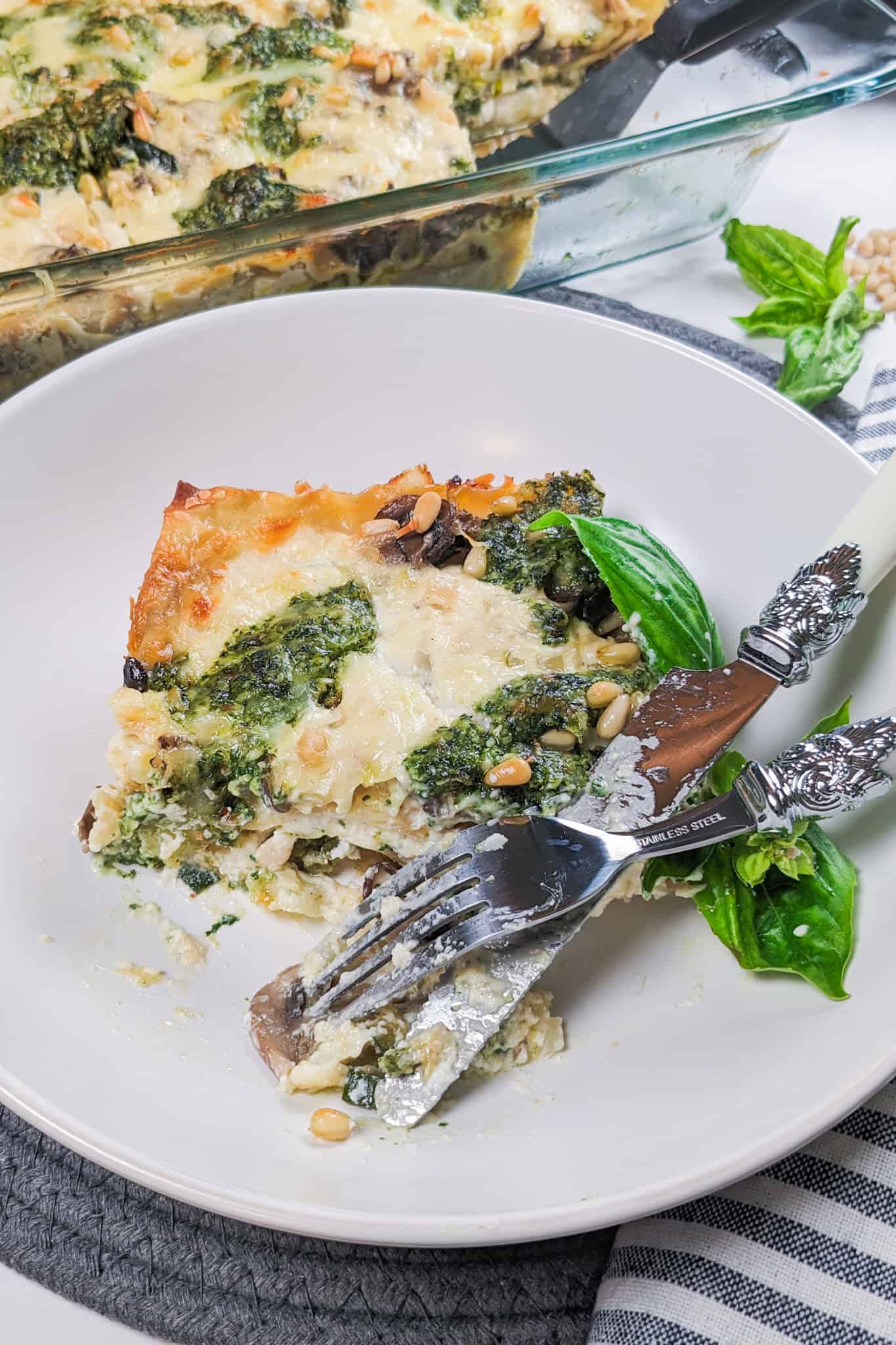 Creamy Spinach Pesto Mushroom Lasagna in a wide rim bowl being eaten with a fork and knife.