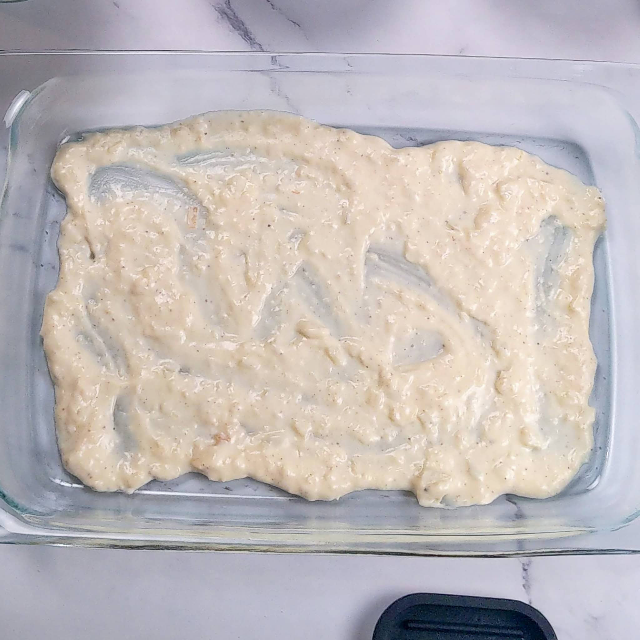 One layer of the creamy onion garlic sauce is spread out evenly on the bottom of the glass Pyrex baking dish.