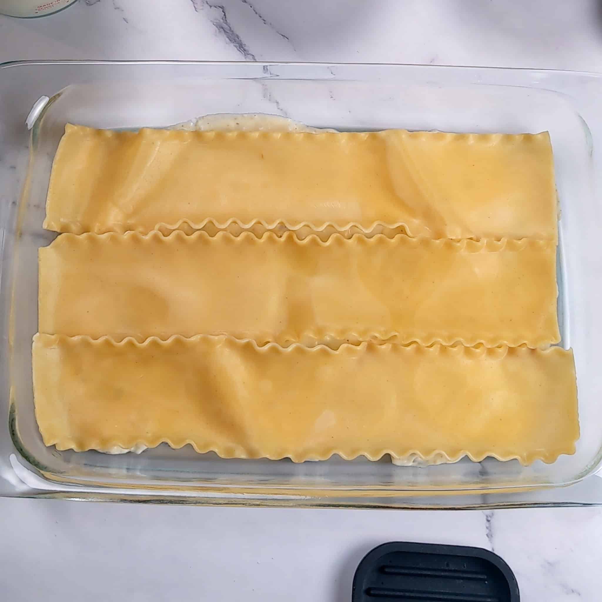 A layer of cooked 3 lasagna noodle sheets side by side in a glass baking dish.