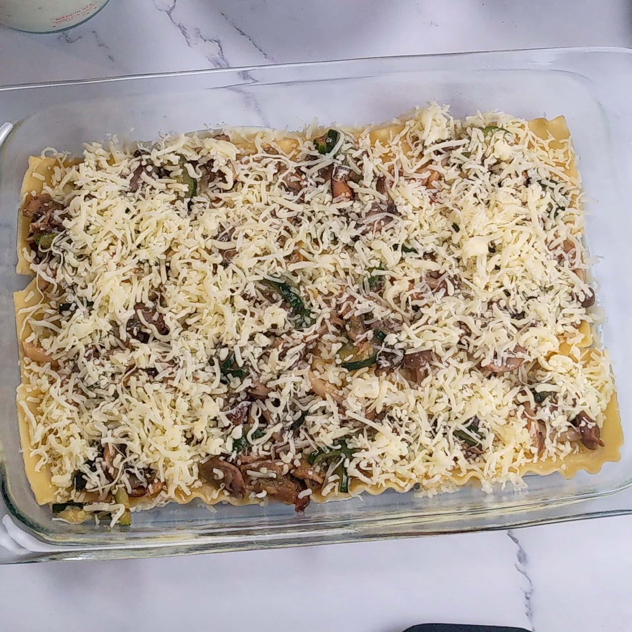 The cooked mushroom and zucchini layer is topped with an even layer of shredded Italian cheese blend.