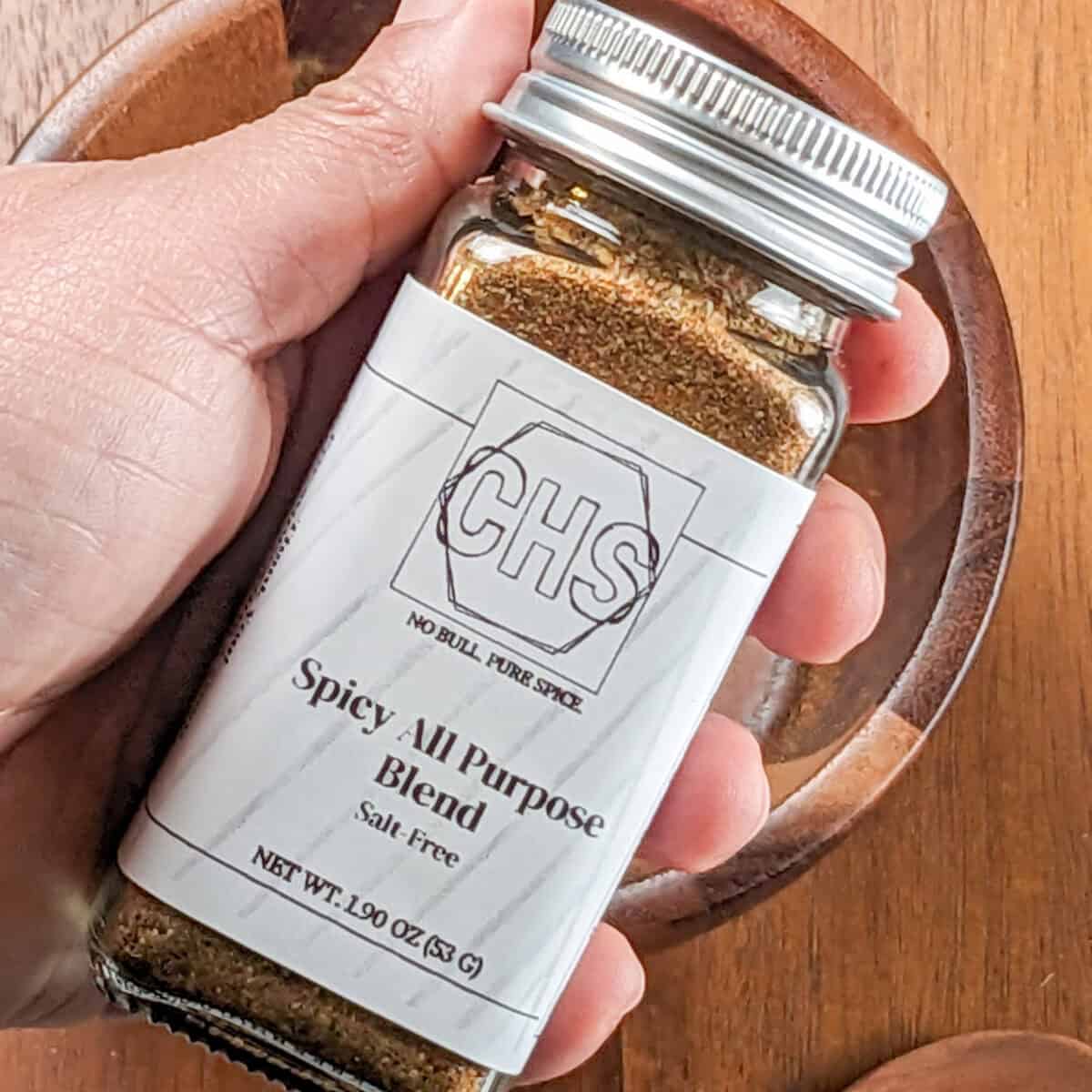 custom herb spice shop's spicy all purpose seasoning blend spice jar held in hand.