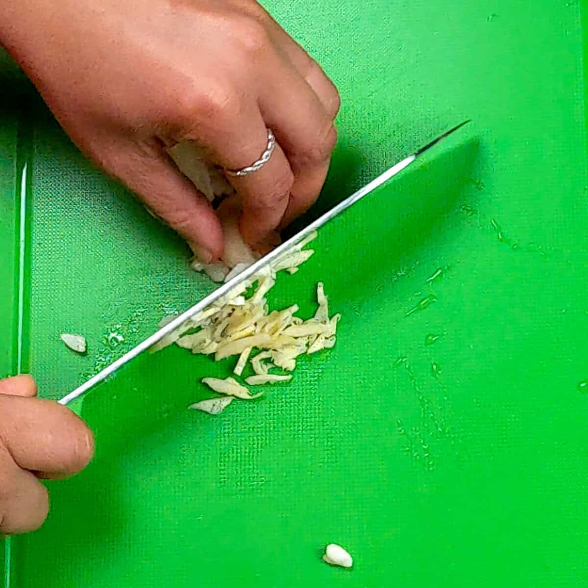 Hand chopping garlic on a green cutting board, showcasing culinary skills and fresh ingredients.