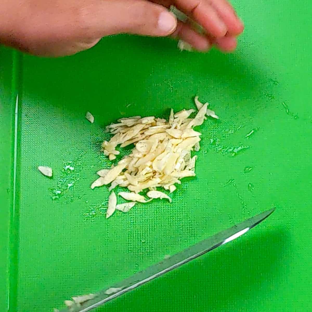 A hand slices garlic on a bright green cutting board.