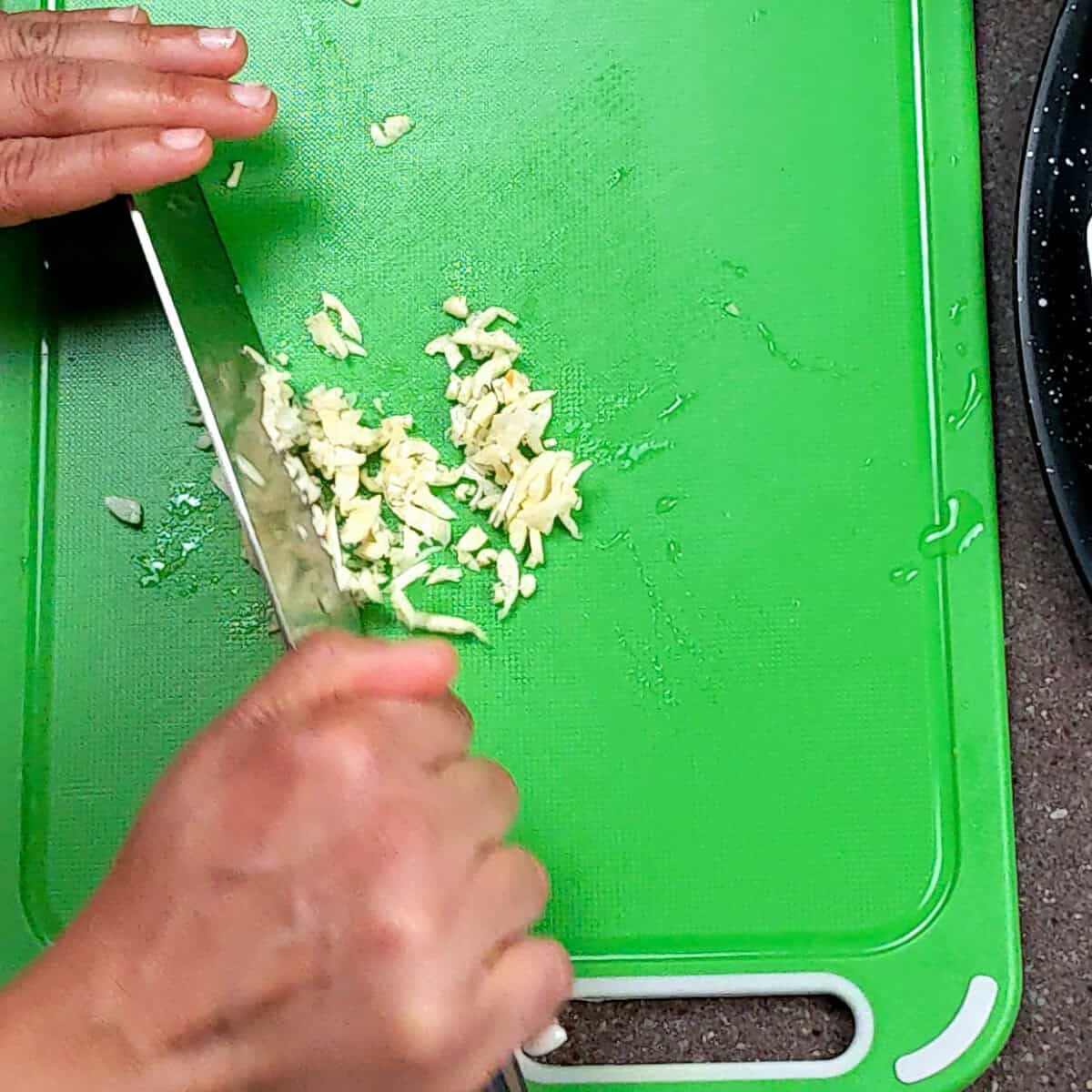 Chopping garlic on a vibrant green cutting board with a sharp chefs knife.