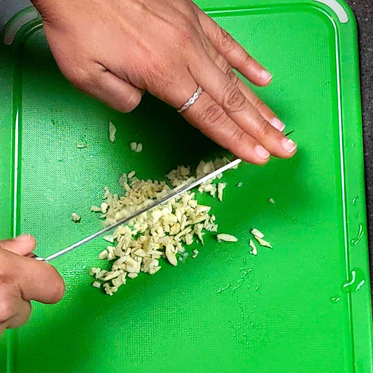 Close-up of garlic chopping on a vibrant green cutting board with a sharp knife.