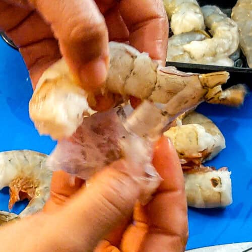 the shell of the shrimp being peel with two hands.