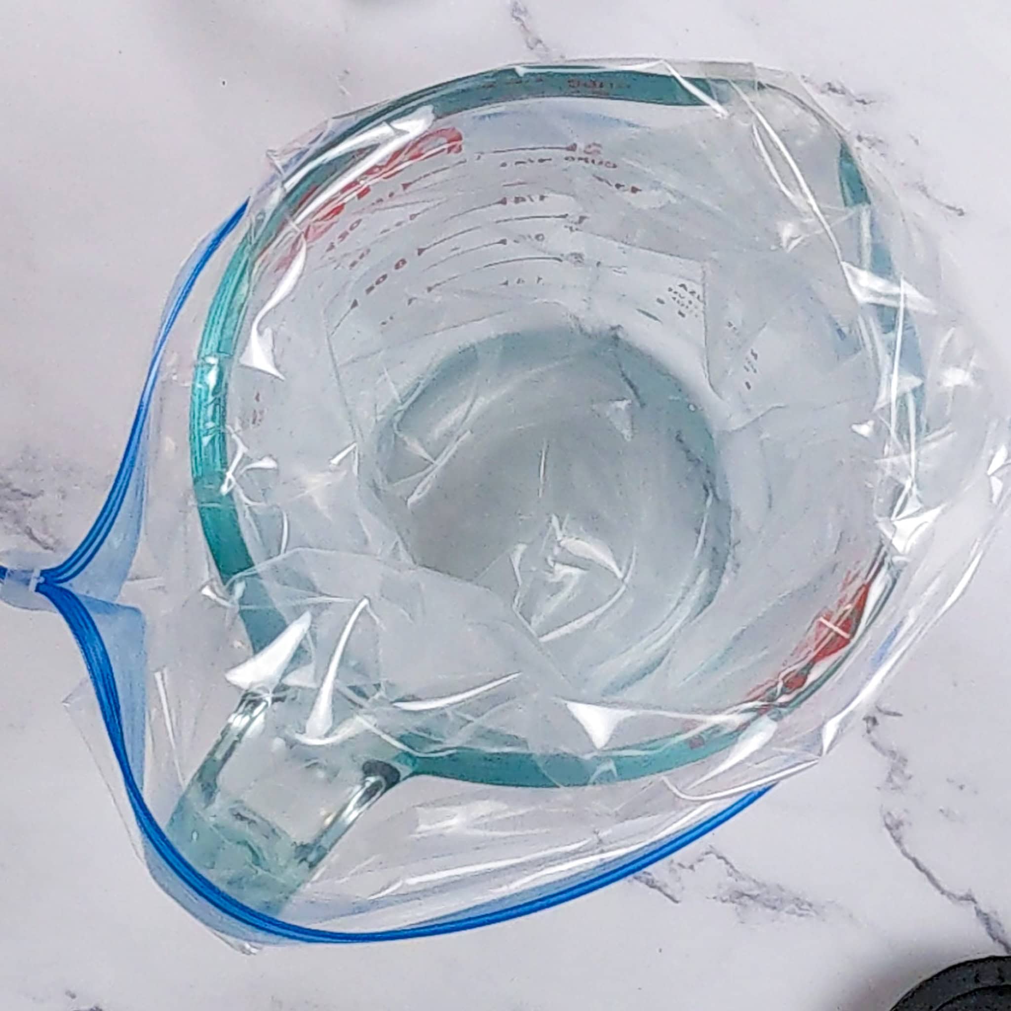 an opened resealable bag pushed into a glass measuring cup.