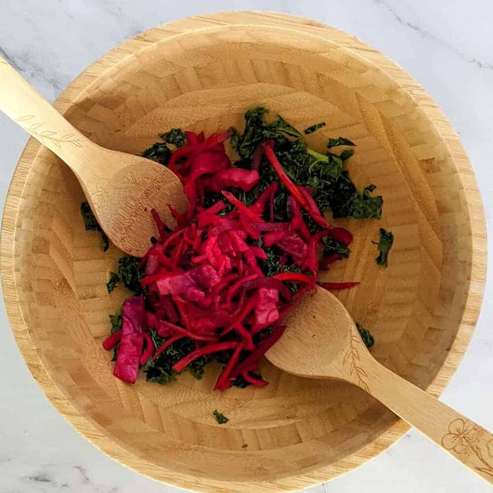 Colorful salad with kale and red cabbage in a bamboo bowl, garnished with wooden utensils.