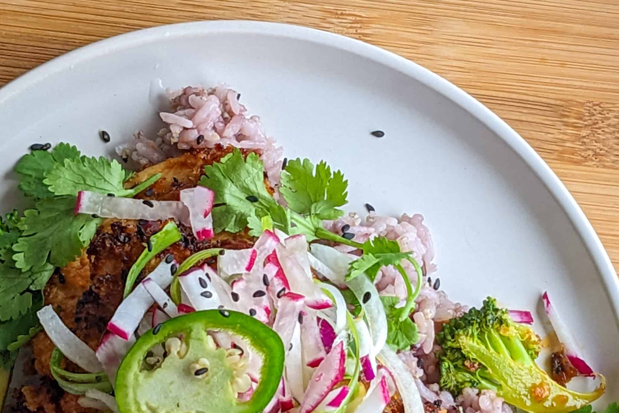 close up the gochujang chicken stir-fry on a round plate topped with vegetables on a bed of multigrain rice.