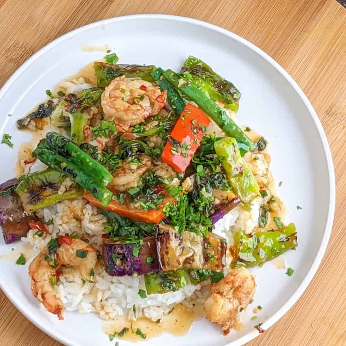 top view of the shishito eggplant shrimp stir-fry over a bed of rice in a flat round plate.