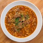 Hearty spicy beef barley stew garnished with fresh herbs, perfect for a comforting meal.