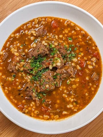 Hearty spicy beef barley stew garnished with fresh herbs, perfect for a comforting meal.