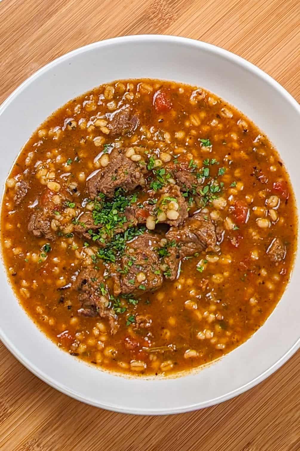 Hearty spicy beef barley stew in a white bowl, garnished with fresh herbs.