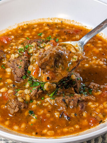 Hearty spicy beef barley stew garnished with fresh herbs, perfect for a comforting meal.