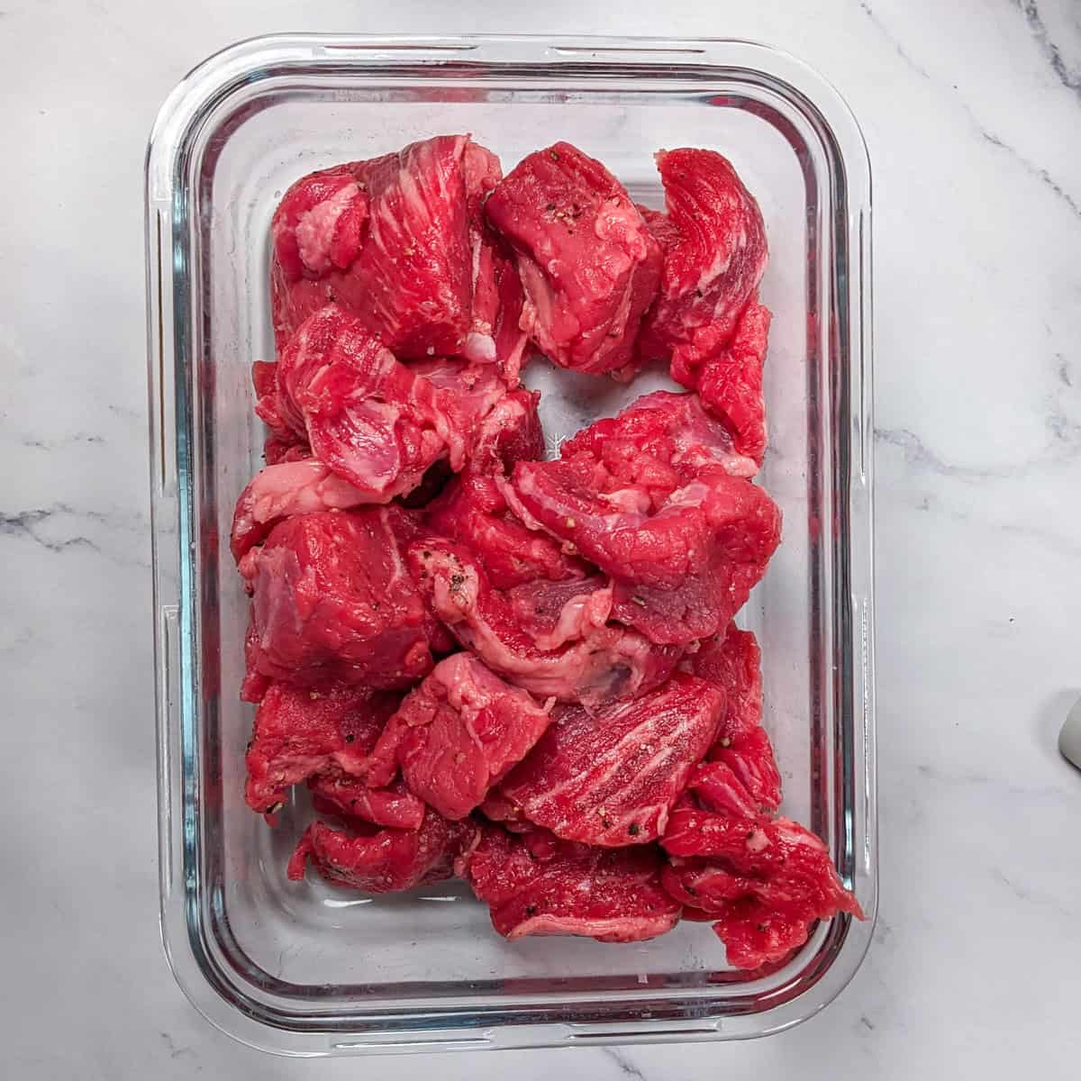 Fresh salt and peppered seasoned beef chunks ready for a spicy barley stew, beautifully displayed on marble.