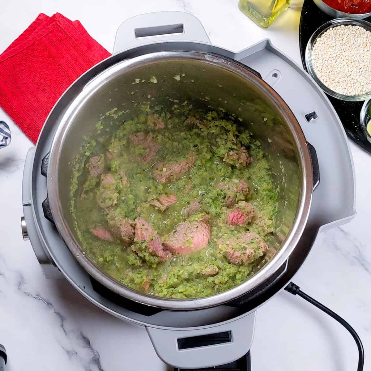 Instant Pot filled with hearty spicy beef barley stew and vibrant pureed green aromatics.