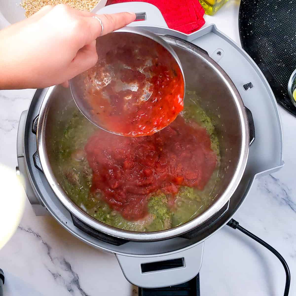 Pouring vibrant red fire-roasted tomato sauce into a pot for delicious beef barley stew preparation.