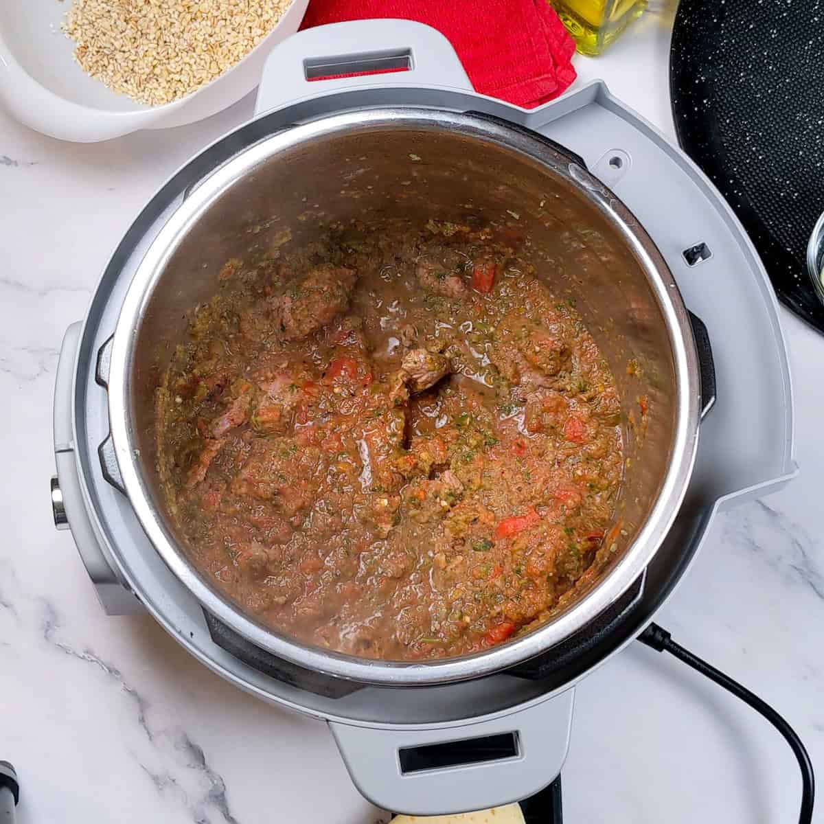 Hearty spicy beef barley stew simmering in a modern multi-cooker on the kitchen counter.