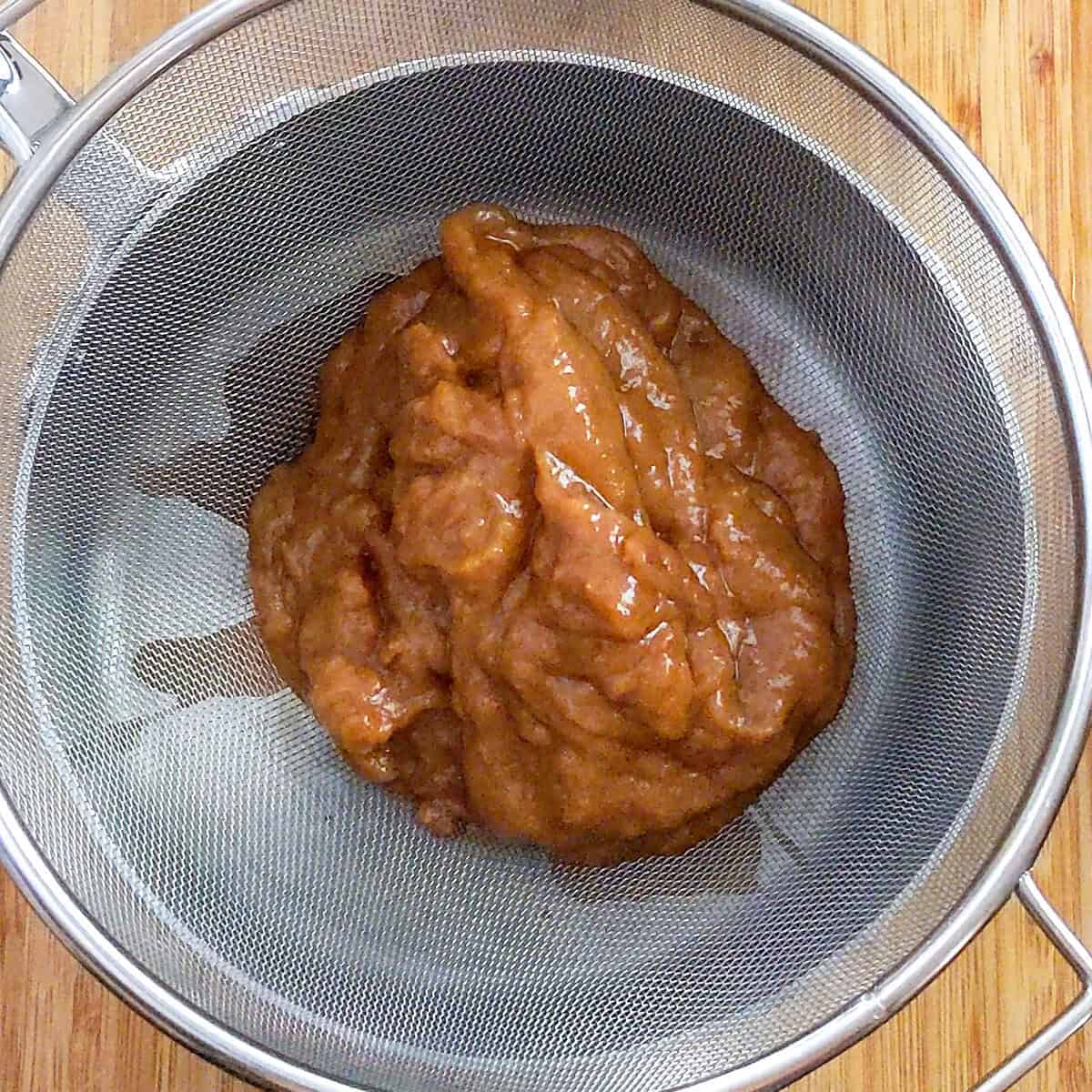 massaged tamarind pulp place in a fine sieve over a sauce pot.