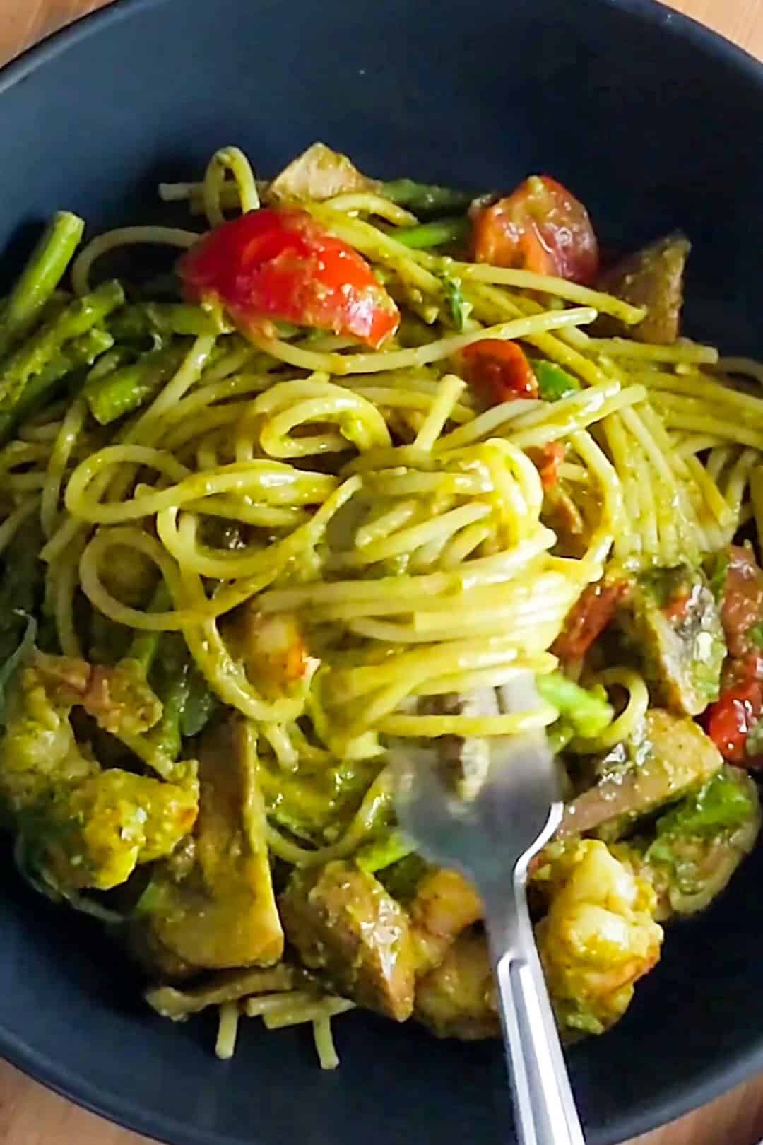 Vibrant Argentinian shrimp pesto pasta with fresh vegetables in a dark bowl.