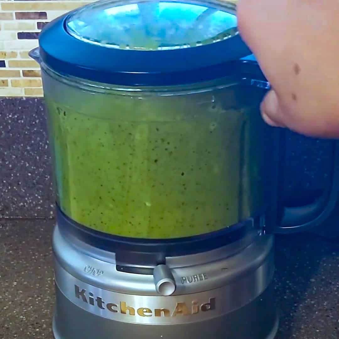 KitchenAid food processor blending fresh green ingredients for Argentinian shrimp pesto pasta.