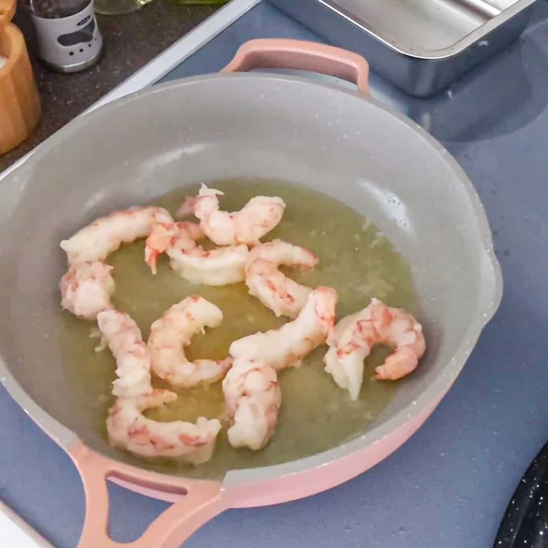 Sautéing fresh shrimp in a pink enameled skillet, perfect for Argentinian shrimp pesto pasta.