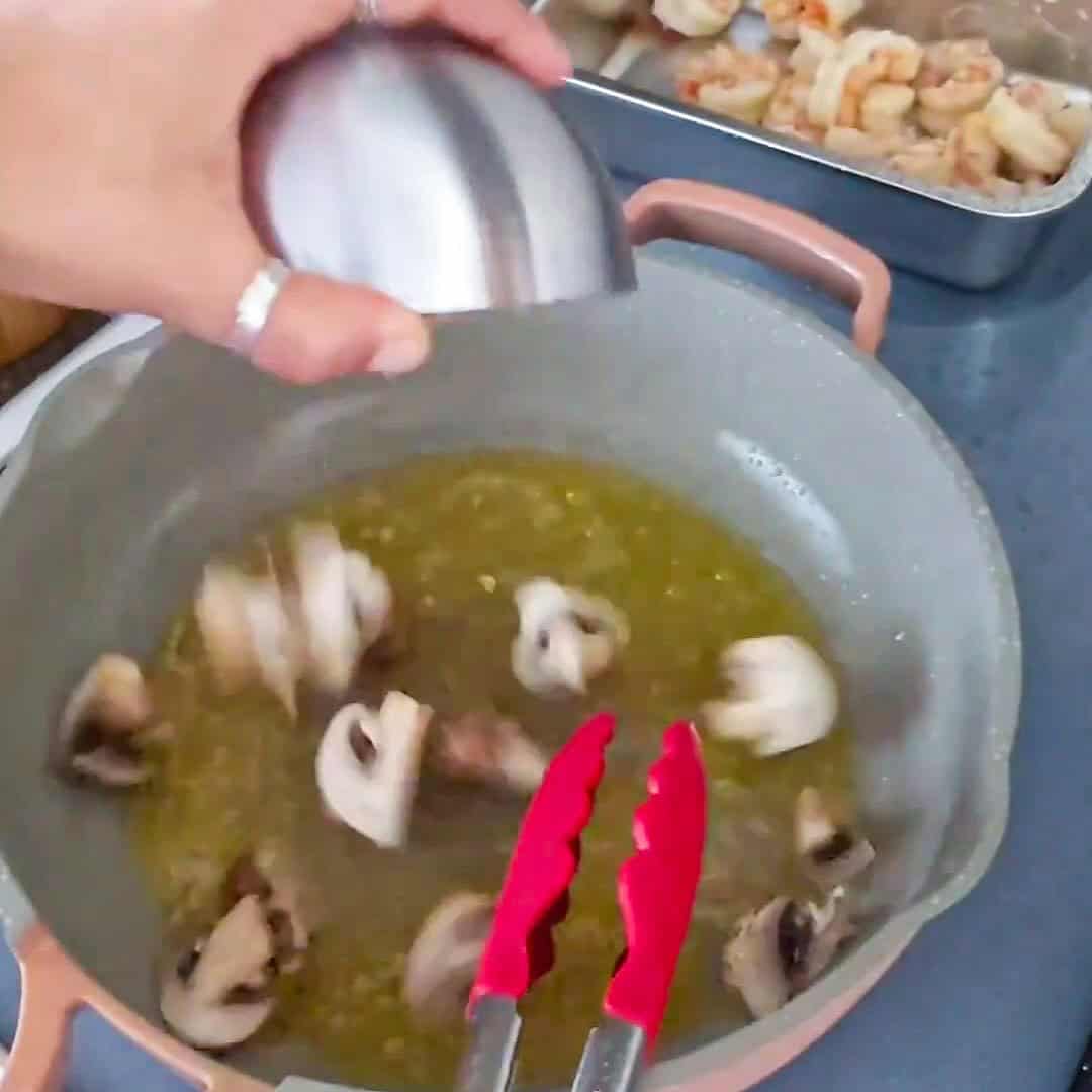 Frying mushrooms for Argentinian shrimp pesto pasta in a vibrant kitchen setting.