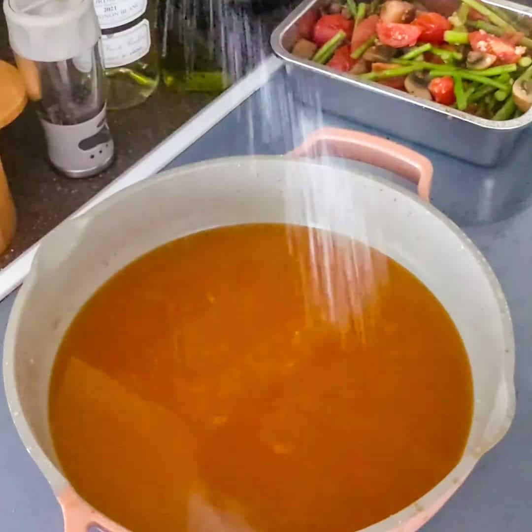 Seasoning a rich broth for Argentinian shrimp pesto pasta with fresh vegetables on the side.