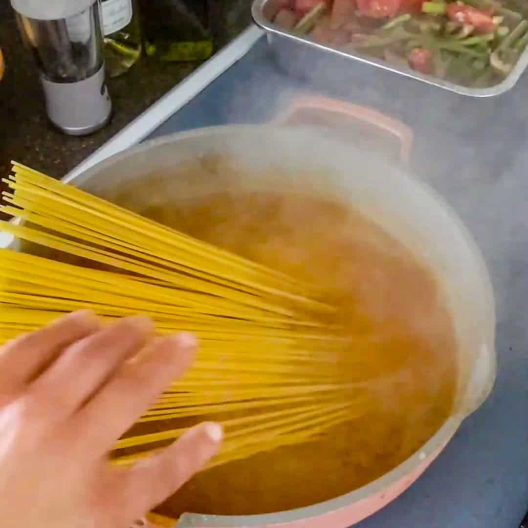 Boiling spaghetti in a vibrant kitchen, preparing Argentinian shrimp pesto pasta dish.