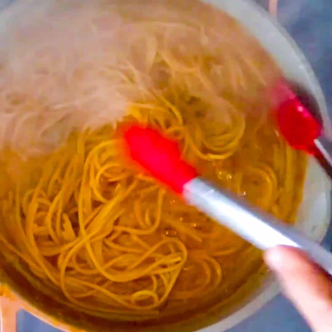 Cooking spaghetti in a boiling pot, using red tongs for perfect Argentinian shrimp pesto pasta.