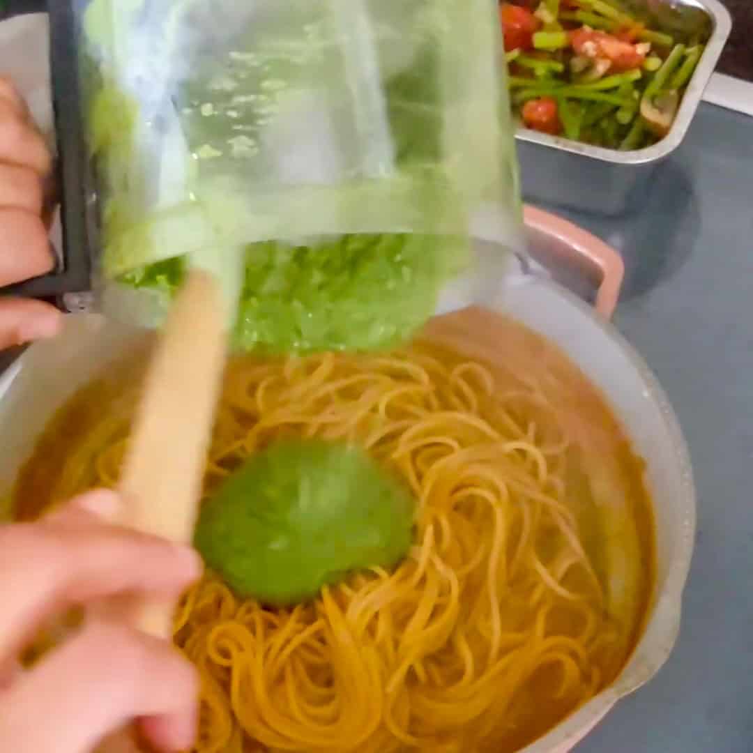 Preparing Argentinian shrimp pesto pasta with vibrant green sauce and tender spaghetti in a cozy kitchen.