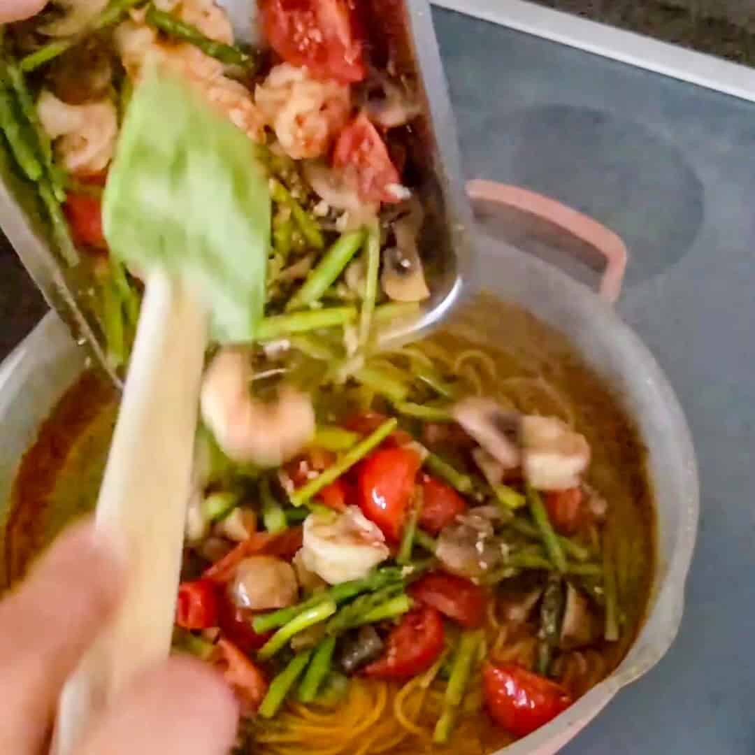 Preparing Argentinian shrimp pesto pasta with vibrant vegetables and flavorful broth in a warm kitchen.