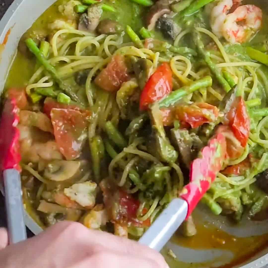 Colorful Argentinian shrimp pesto pasta with asparagus, tomatoes, and mushrooms in a vibrant dish.