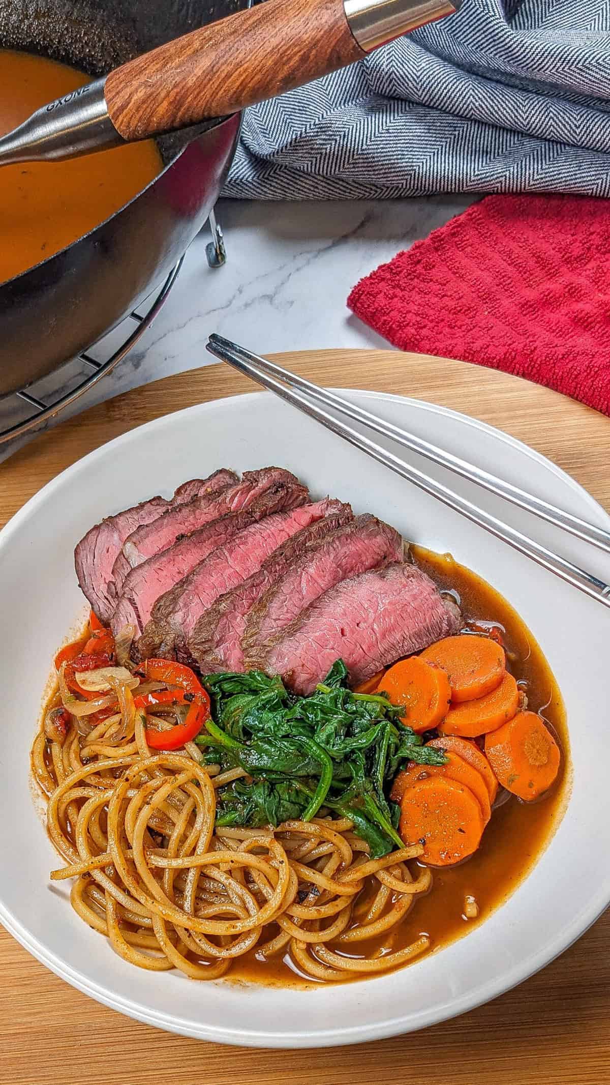 Delicious Caribbean beef noodle soup with vibrant vegetables and tender roasted beef slices.