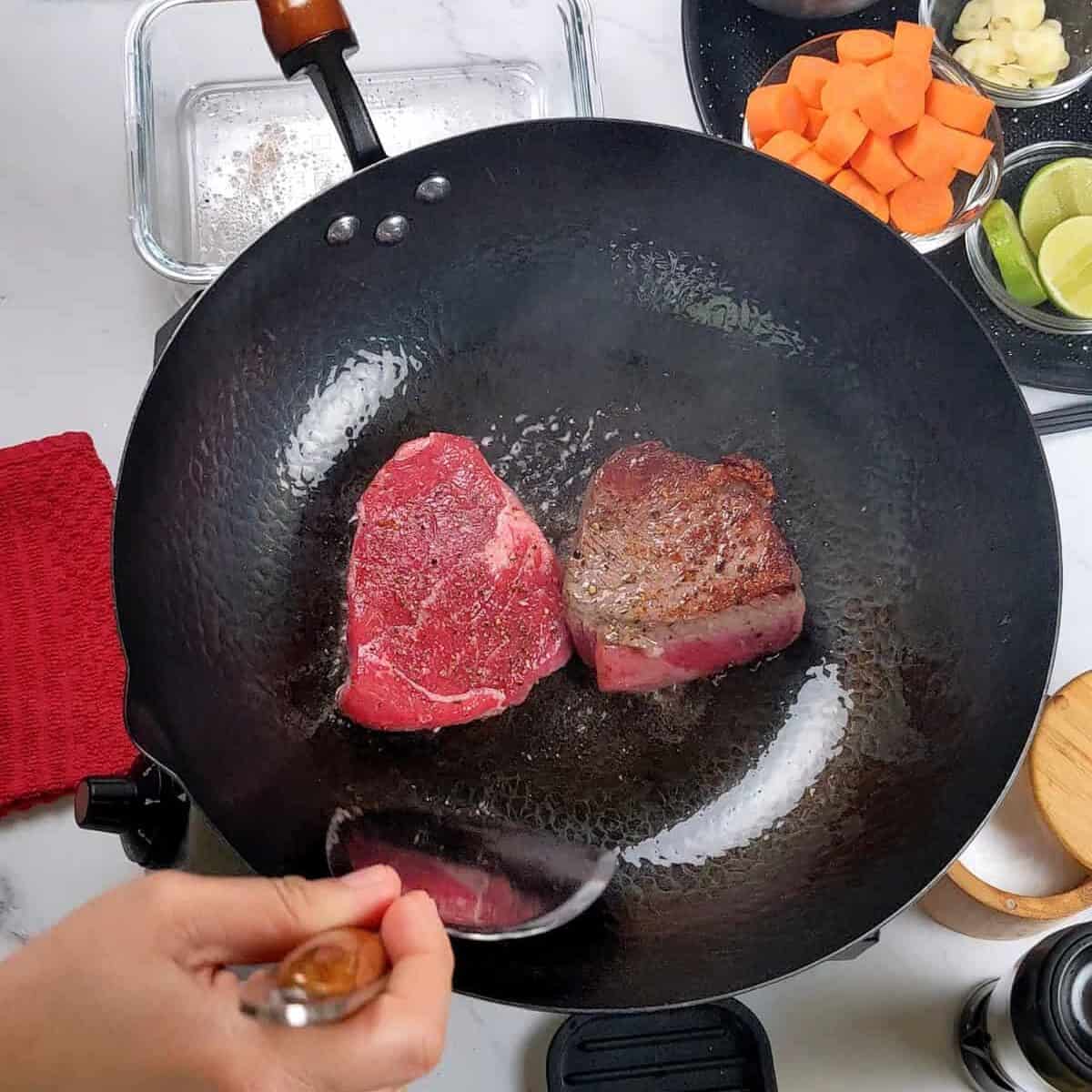 Sizzling beef being prepared in a wok for Caribbean beef noodle soup, with colorful vegetables.