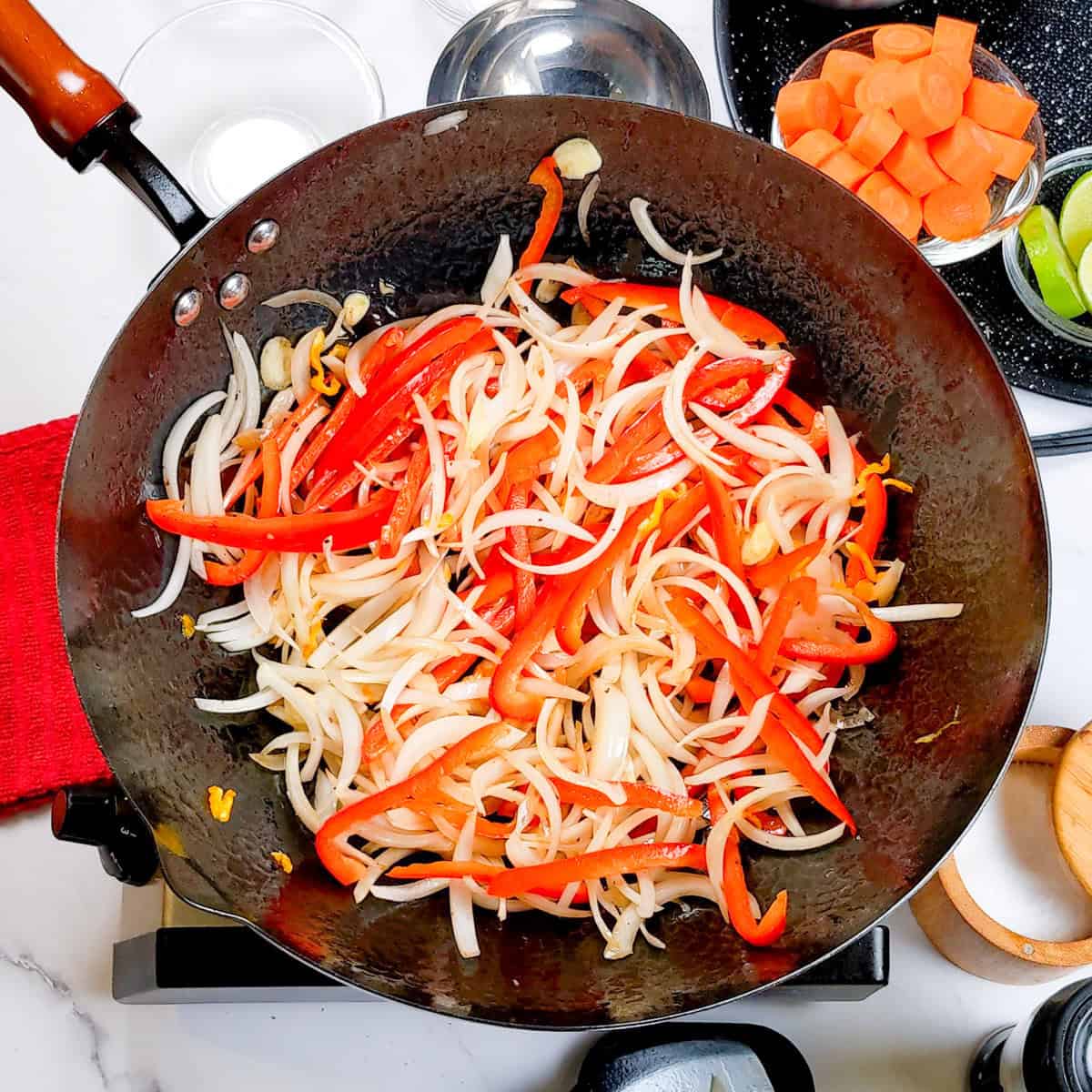 Sautéed vegetables in a seasoned wok for Caribbean beef noodle soup cooking step.