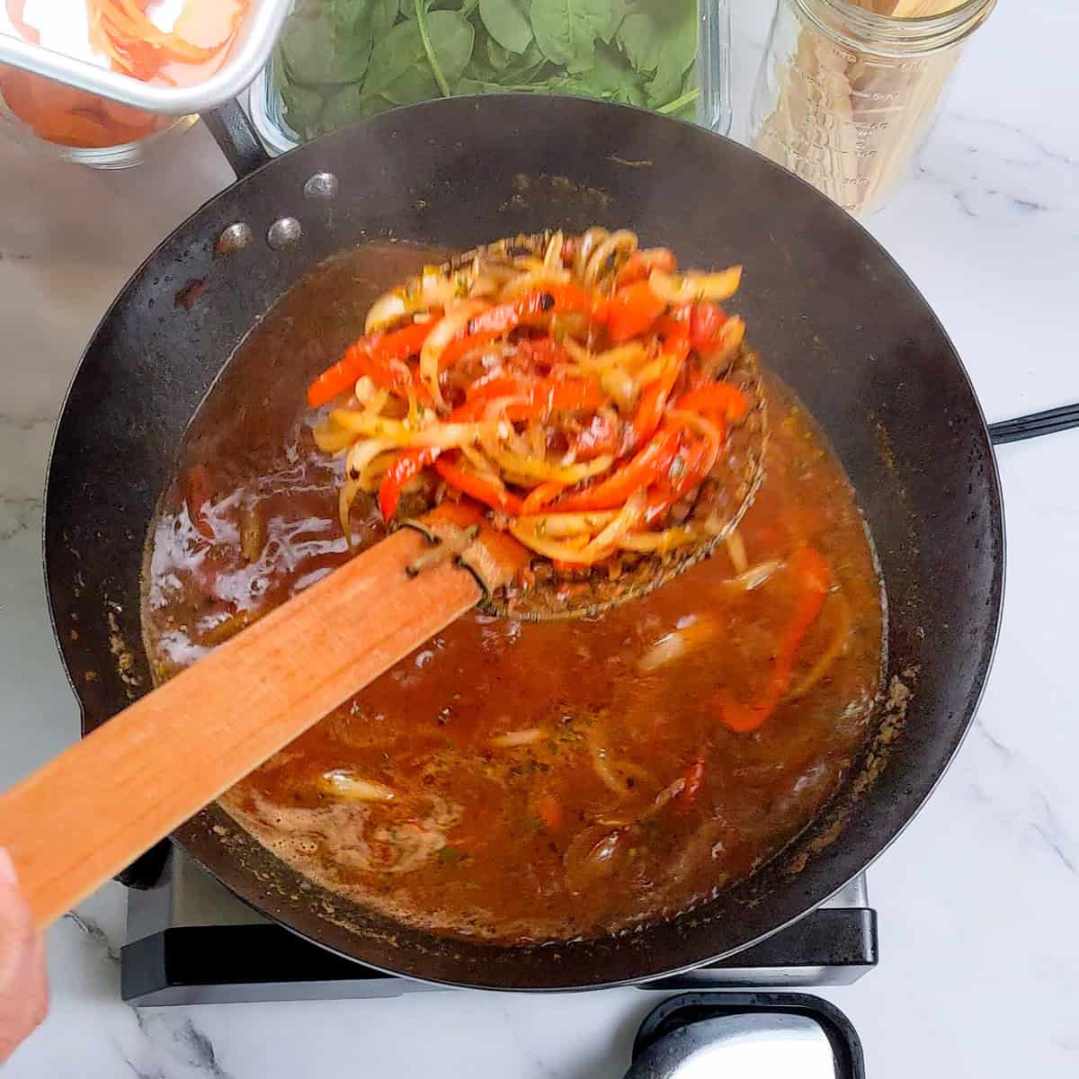 Vibrant Caribbean beef noodle soup in a wok with sautéed peppers and fresh ingredients.