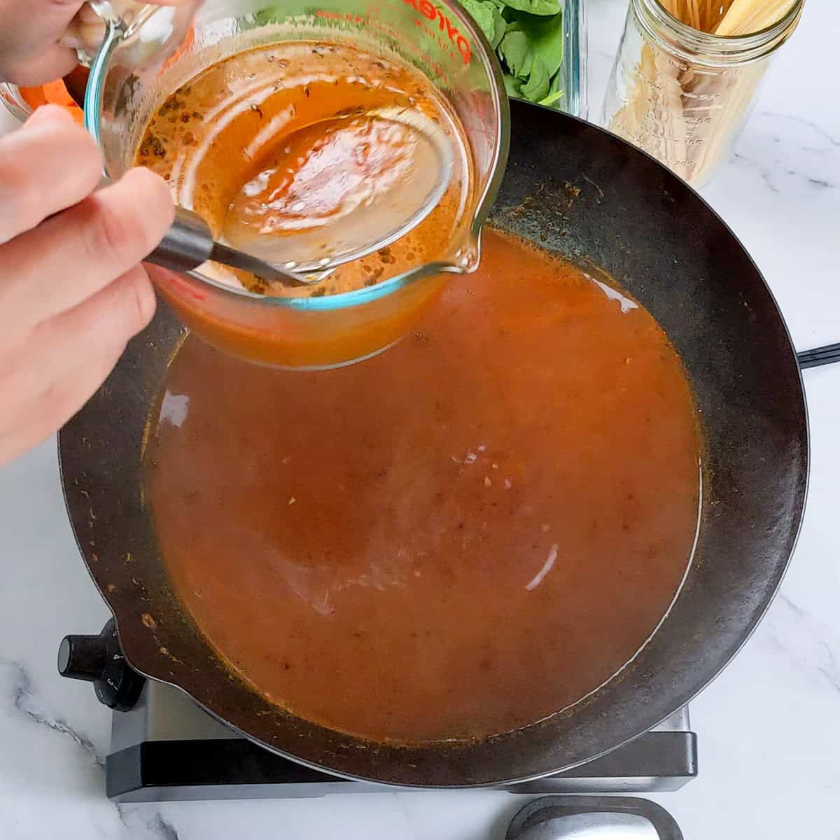 Pouring broth into a wok for Caribbean beef noodle soup preparation.