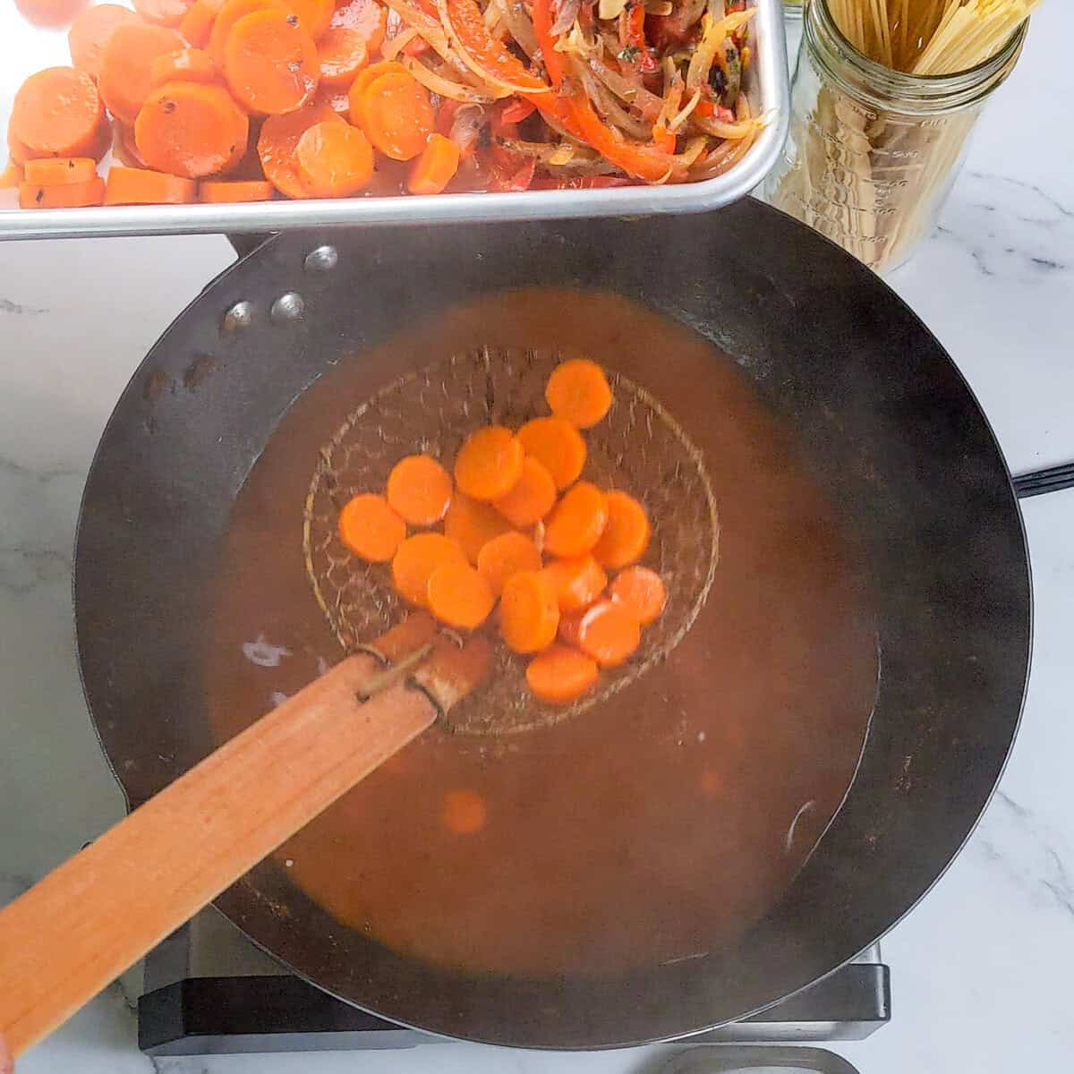 Caribbean beef noodle soup simmering in a skillet with fresh carrots ready to add.