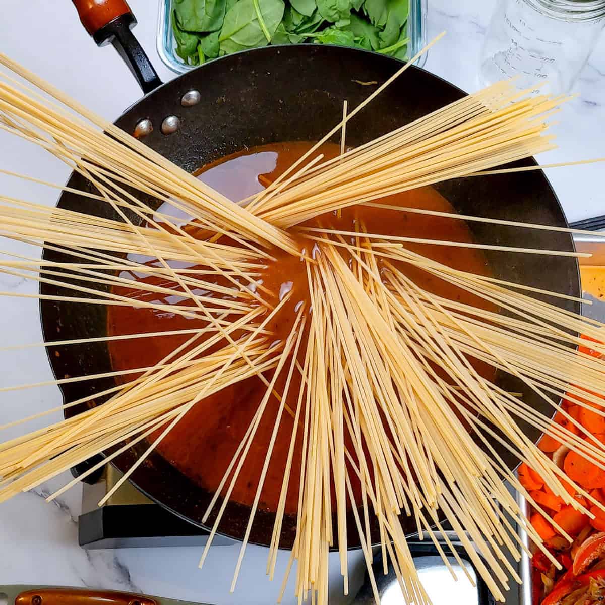 Vibrant Caribbean beef noodle soup with spaghetti and fresh spinach in a skillet.