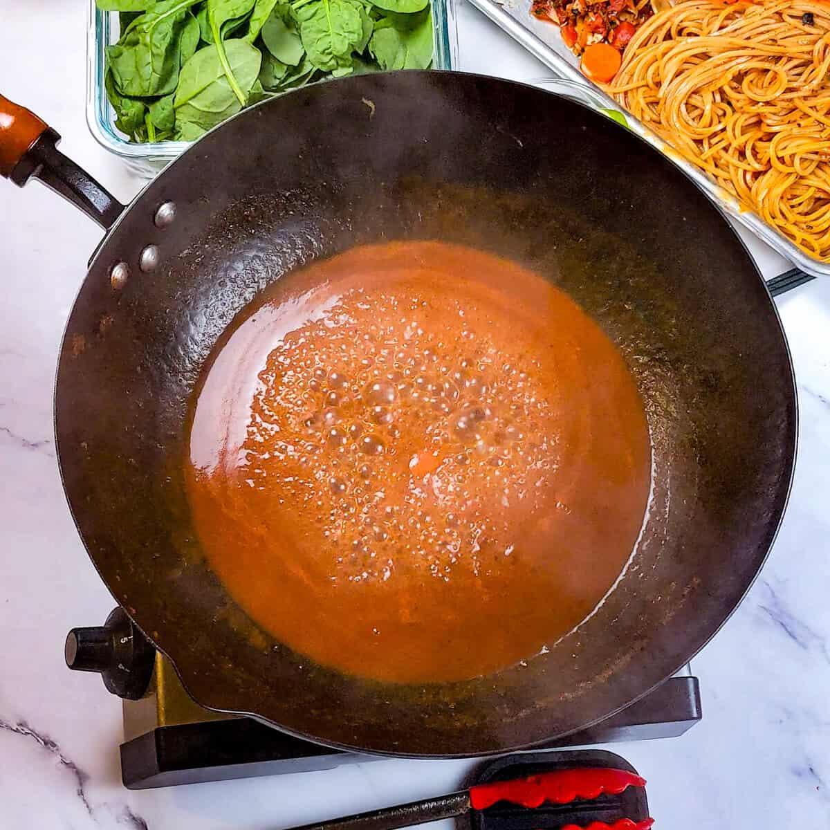 Rich Caribbean beef noodle soup with vibrant greens and seasoned sauce in a wok.