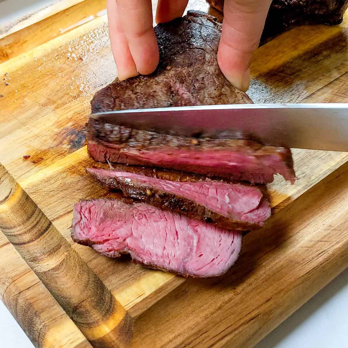 Perfectly sliced medium-rare beef on a wooden board, showcasing delicious Caribbean Beef Noodle Soup.