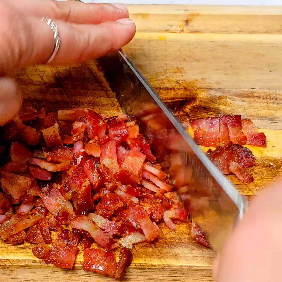 Chopping crispy bacon on a wooden cutting board in a cozy kitchen setting.