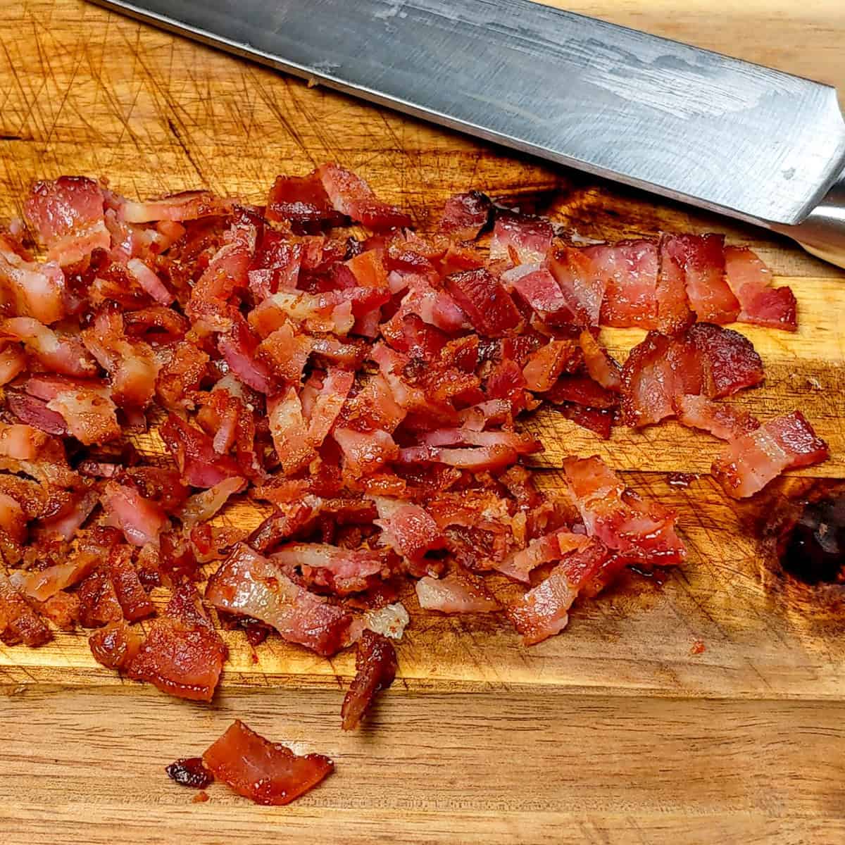 Chopped bacon on a wooden cutting board with a sleek knife ready for cooking.