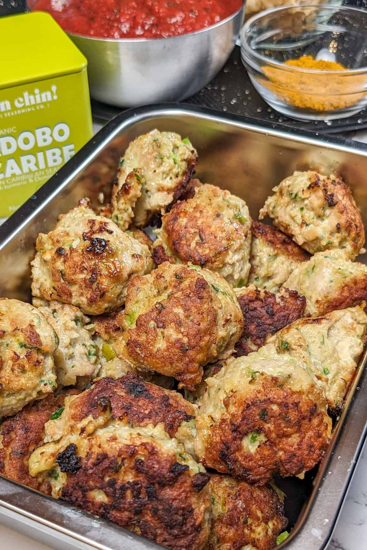 Curry turkey meatball soup in a stainless-steel tray with vibrant sauce and spices.