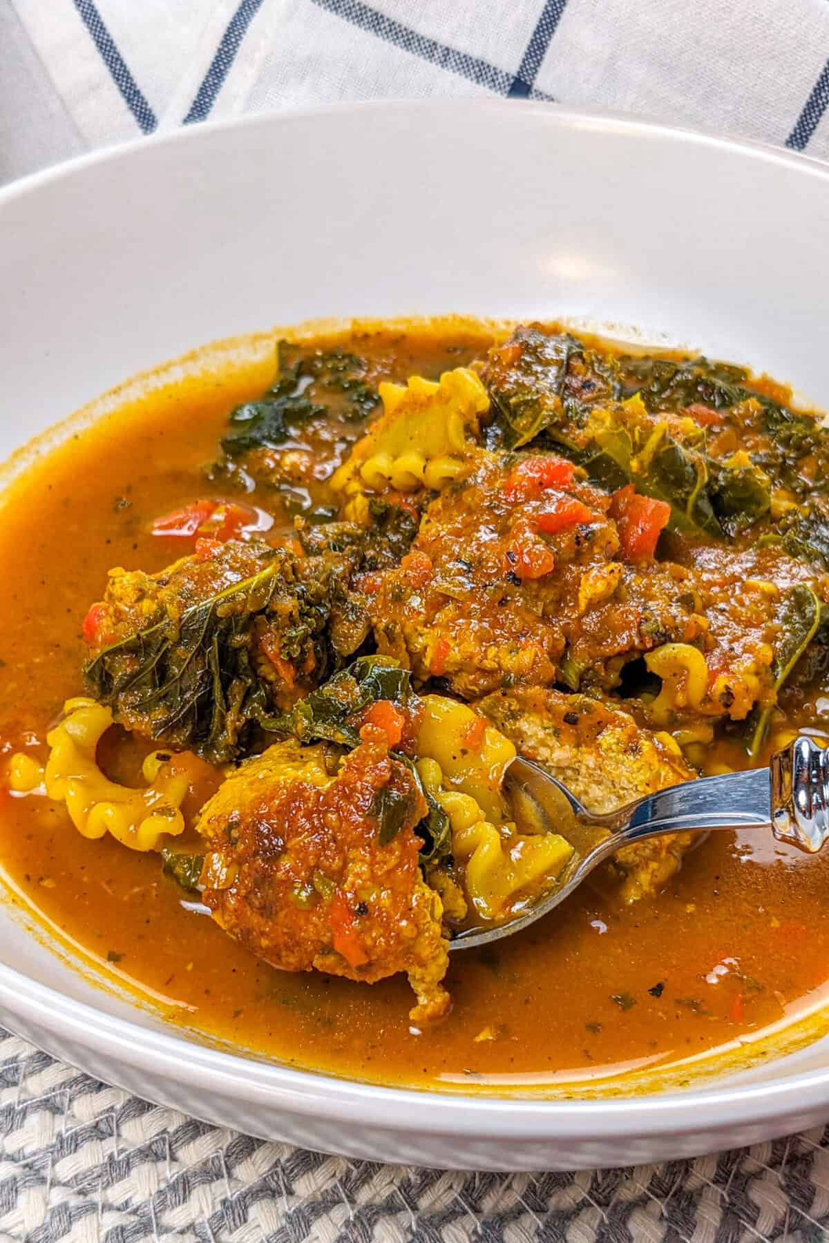 Hearty curry turkey meatball soup with vibrant vegetables and greens in a comforting broth.