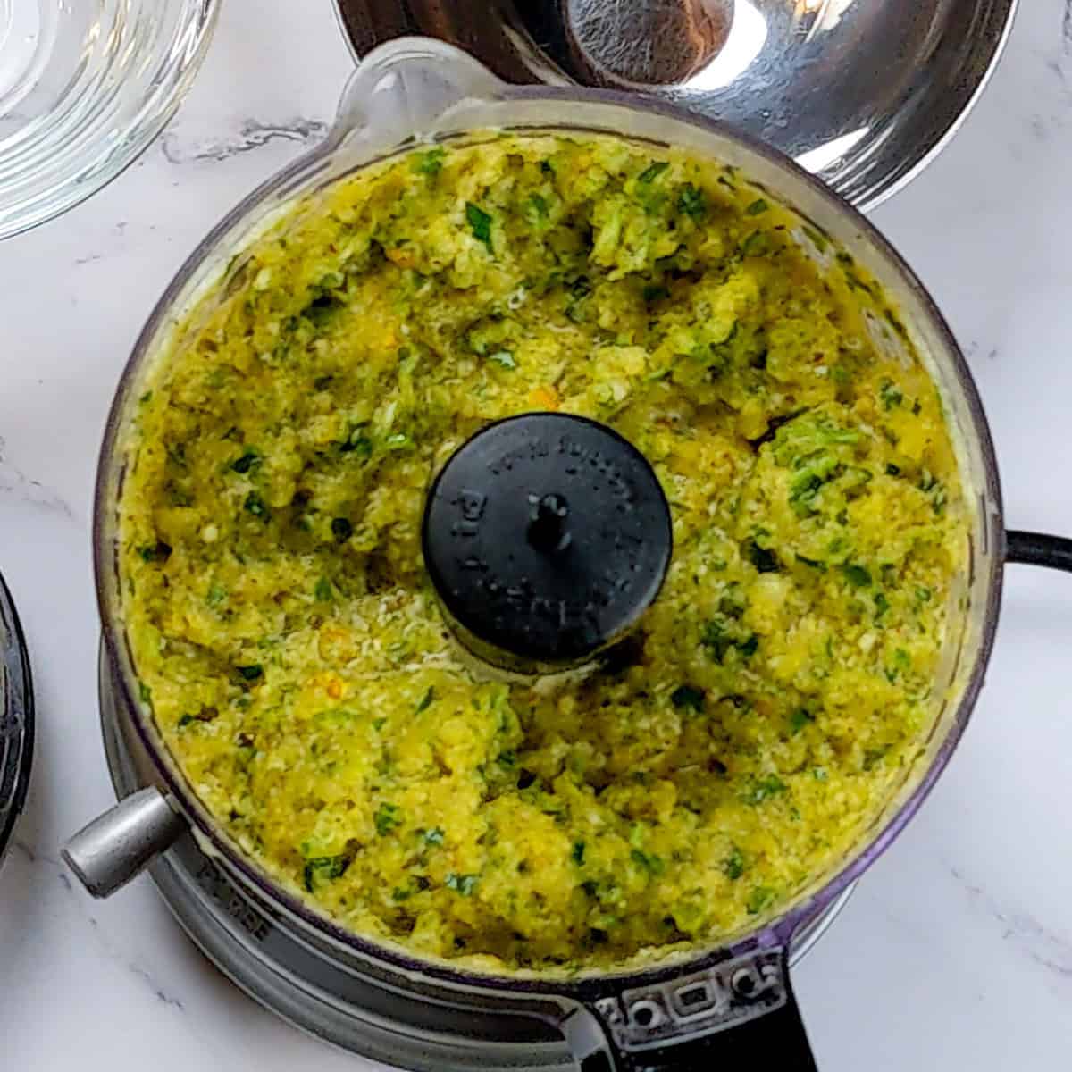 Vibrant fresh vegetable mixture in a food processor for curry turkey meatball soup.