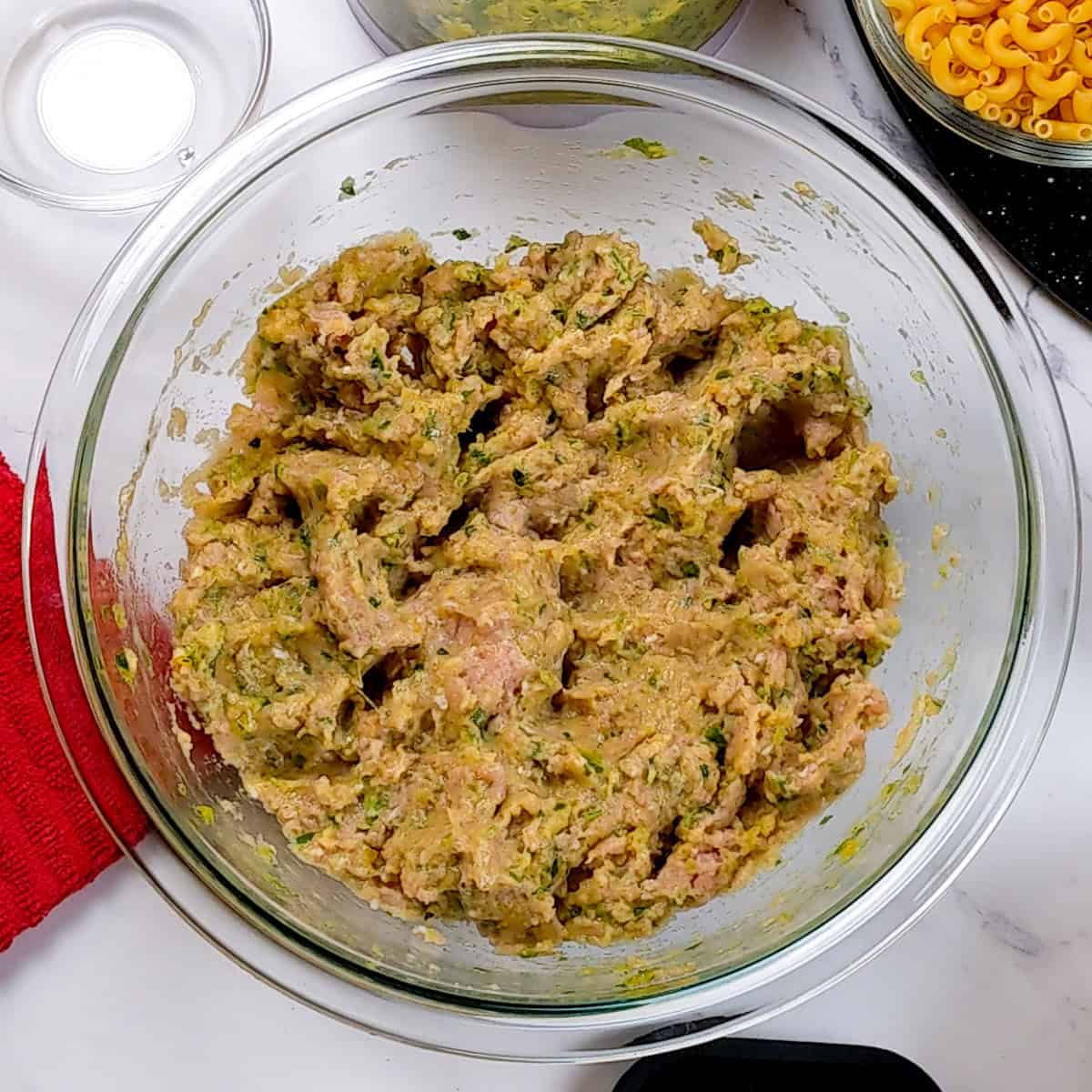 Chunky turkey meat mixture in a glass bowl, ready for curry meatball soup preparation.